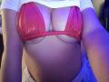 AntoniaBrunni in a red mesh bikini top, showing her big tits, with her white shirt pulled up, under blue lighting, exposing her belly and a bit of her ass.