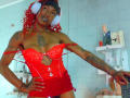 DaniaMarcell with red curly hair, wearing white headphones, red lace corset, and matching red skirt, exposing small tits and tattoos, standing in a bathroom with sex toys.