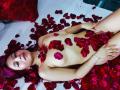 ShofiaWett, nude, with red petals covering her tits and pussy, lying on white bed, pink hair, bracelet, necklace, red pillow, looking at camera, sexy, cute, relaxed.