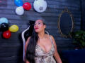 VictoriaKiley with big boobs in a leopard print dress, long black hair, red lipstick, sitting on a chair, colorful balloons, and an ornate mirror in the background.
