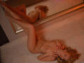 ElinNorr, nude with blonde hair, lies on white carpet, legs up, reflecting in mirror, hands on chest, small tits, soft lighting, silver bracelet, relaxed expression, warm orange glow.