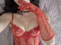 Rozalin with red lace lingerie, sheer red gloves, black choker, and dark wavy hair, touching her red lips. Her boobs are visible through the lace, showing some cleavage.