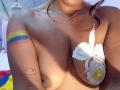 Caylin's topless with large tits, white flower covering one, yellow and blue flag tattoo on arm, map tattoo on shoulder, gold necklace, brown hair, sunlit skin.