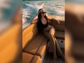 MiilaWx with big tits, wearing a black top and patterned pants, lounges on a boat, arms resting, sunglasses on, gold headband, and wavy brown hair, by the water.