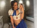 ElwandaKiehne in a sailor outfit with puffy sleeves, blue skirt, and anchor top, showing her small tits and black bra, holding a phone, tattoos visible on her arm.