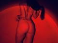 Tisia's ass is in a red thong, her back to the camera, holding her ponytail. She's wearing a matching red bra, illuminated by red light.