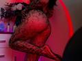 Tsukerberg's butt in a black lace fishnet, standing on one leg, with red lighting highlighting her curvy, sexy body. Her hand touches her back, showing off her figure.