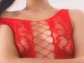 MilaHans wearing a red, diamond-patterned, fishnet lingerie top, exposing her tits through the open weave. Her arms are crossed, highlighting her chest.