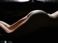 KamiLove's smooth, curvy ass and back are illuminated by soft light, highlighting her pale skin against a dark leather surface. Her body is in a lying down position.
