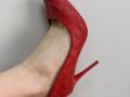 Tattiya's leg in a red, woven high heel with a stiletto heel, showing her pale skin and visible blue veins. The shoe is partially on her foot.