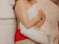 StephanieSun with red lace panties, holding a white fluffy pillow, covering her tits, wearing a watch and necklace, sitting on a white textured bed.