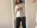 Elliance with medium tits, brown hair, white blouse, black pants, standing in front of mirror, hands on blouse, slight frown, reflection shows her from front.