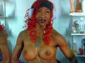 Topless DaniaMarcell with red curly hair, wearing white headphones, tattoos on chest and arms, dark lipstick, medium-sized boobs, looking at camera in a bathroom with sex toys.