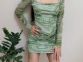 AmeliaMaiv wearing a green, marble-patterned, long-sleeve mini dress, her hand on her hip, showing her ass, next to a green plant. Her ring is visible.