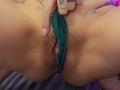 Les culottes en dentelle verte d'ElixirShanna sont tirées sur le côté, exposant sa vulve poilue avec des lèvres visibles. Sa main tatouée avec des ongles roses tire sur les culottes..