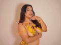 ValeryRiven with yellow tape covering her tits, holding one hand near her mouth, long dark hair, light skin, and a tattoo on her right side, against a plain background.