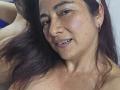 Alessia, capelli castano scuro, viso lentigginoso, piccoli orecchini a cerchio e un leggero sorriso, in un selfie che mostra la parte superiore del corpo e i seni scoperti, appare rilassata..