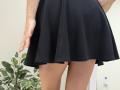 Rorria's black skirt, showing her bare, tan-skinned thighs and buttocks, with a slight, textured fabric, and a green potted plant in the background. Water bottle bottom right.