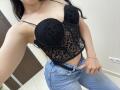 OliviaGranda with black lace and leopard print bustier, showing her tits, wearing blue jeans, black belt, and silver bracelet, taking a selfie in a white room.