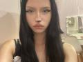 CherelleGess has long black hair, big black eyeliner, and pouty lips, wearing a black lace top. She's looking at the camera with a serious expression.