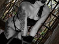 NenaBlack with black lingerie, tattoos covering her arm and side, black mask, and necklace, bending forward, showing her tits and pussy, in a gritty, dark, urban setting.