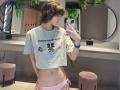 ErynAttridge stands in front of a mirror, holding a phone, wearing a gray crop top with "boom pants over" text and pink string bikini bottoms. Wet brown hair, slim physique, sexy.