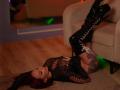 TorriKitt with red hair, black lace top, and thigh-high black boots, lying on the floor with legs on a couch, showing tattoos and her ass.