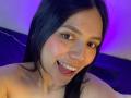 SophiaMarx has black hair, a light skin tone, small tattoos on her neck, and is smiling with her tongue out, showing her teeth. Purple lighting highlights her face.