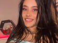 KarolPalacios with long black hair, pink eyeshadow, nose ring, smiling with white teeth, wearing a green and white striped top, showing cute ass in the mirror reflection.