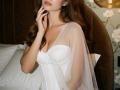 Diantrisy with long brown hair, wearing a white strapless dress with a sheer cape, touching her face, showing her tits and a sexy, gentle expression.