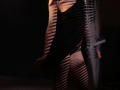 TriciaBarnes with her back to the camera, wearing a black dress, her bare ass and pussy slightly visible through striped shadows. Dark, moody lighting.