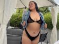 AntonelaVega standing outdoors, wearing black sheer bra and lace thong, denim jacket open, exposing her large tits and curvy ass, black hair, smiling, white canopy, green bushes.