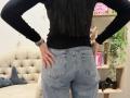 Dalaila's ass in tight blue jeans, hands on hips, black long-sleeve shirt, wristwatch, and ring, standing with back to camera, showing her butt pockets.