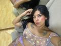 Catalina Reiyna está deitada em um sofá, vestindo um conjunto de lingerie lavanda transparente com estampas de margaridas, expondo seus seios grandes e tatuados e uma calcinha de renda roxa. Seu rosto tem um rubor avermelhado..