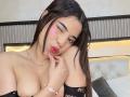 LunaVali with puffy pink cheeks, winking, wearing black fishnet sleeves, and a necklace, biting her finger, showing off her small tits and a bracelet.