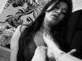 AbbyNdYliria with long dark hair, eyes closed, face showing pleasure, being touched on chest by someone's foot with a flower tattoo. Black and white photo.