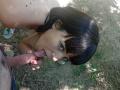 OrianaAndFriends with dark hair, looking up, sucks a man's cock. Her pink nail-polished hand grips the shaft. She's outdoors, topless, with a visible mole on her shoulder.