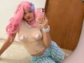 LiMiuu with pink hair, wearing a sheer top with nipple pasties, blue and white patterned skirt, holding a pink phone, mirror selfie, showing her tits, pink hairclip.