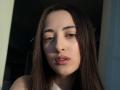 BokSinha has long brown hair, light skin, and full pink lips with a slight pout. She's looking down with soft, brown eyes, and her face is lit by sunlight.