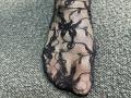 Tattiya's foot is covered in black lace with intricate floral patterns, showing her toes through the sheer fabric. The lace is tightly woven, highlighting her skin.