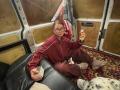 HotCaramelsTrio with glasses, red track suit, holding beer, sitting on black leather couch, patterned rug, white and black shoes, beige socks, holding a game controller, inside a van.