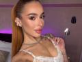 MarissaFex has tan skin, long brown ponytail, and wears a white lace bralette. She's showing off her small tits with a hand, sporting a choker, and has tattoos.