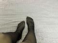 Les pieds de Destinis, portant des collants noirs transparents, les orteils légèrement écartés, reposent sur une couverture blanche texturée. Le motif des collants visibles met en valeur la peau pâle de Destinis..