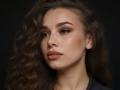 Niferttiti has wavy brown hair, full eyebrows, and pouty lips with nude lipstick. Her skin is smooth and she's looking slightly to the side with a calm expression.