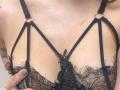 I seni di MoonLiza, in pizzo nero e lingerie con dettagli a spallina, anelli dorati e motivi floreali, sono tenuti dalla sua mano, con unghie naturali, mostrando una piccola cicatrice sul petto..