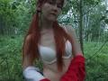 SheritaChieng with red pigtails, white bra, and red jacket, sitting in a forest, showing her small tits and fair skin. She has a neutral expression and green leaves around.