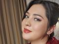 PaulaAnd has dark brown hair, red lipstick, and gold earrings, smiling with slightly tilted head, brown eyes, and subtle eyeliner. She's looking to the side with a cute expression.