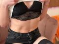 Sanella's small, black lace bra cups her tits, showing a bit of her flat, toned stomach. She's wearing black denim shorts and a white ribbed shirt.
