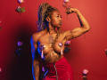 DaniaMarcell with braided hair flexing arm, topless with heart pasties covering her tits, red leather skirt, tattoos, and roses in the background, posing confidently.