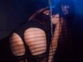AgataRyili in black lace panties, bending over with her big ass in focus, striped shadows on her skin, a silver chain in the foreground, dark and moody lighting.